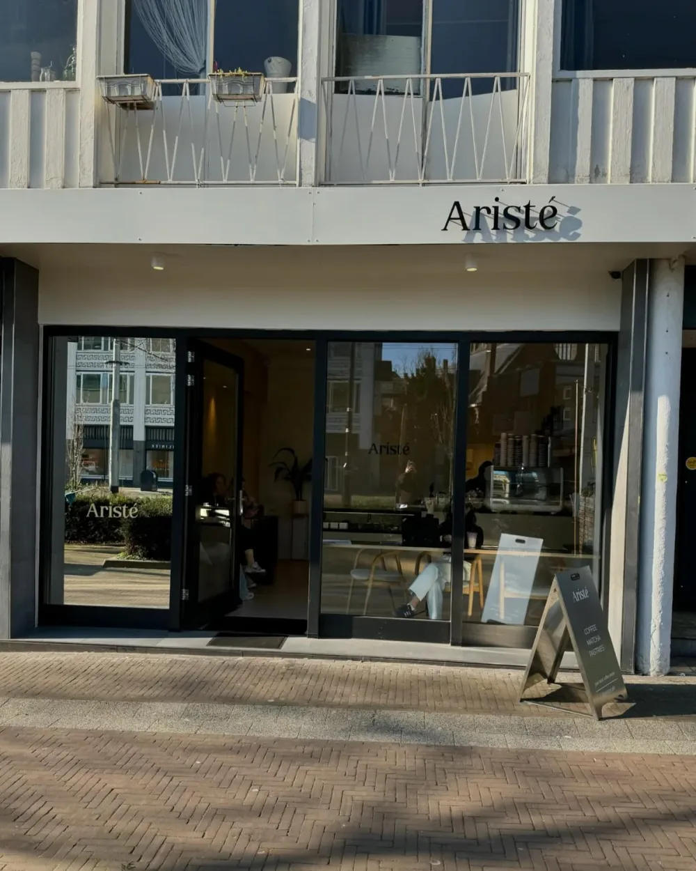 De gevel van Aristé aan de Ir. J.P. van Muijlwijkstraat in Arnhem, met de naam op de luifel en een trottoirbord op de stoep
