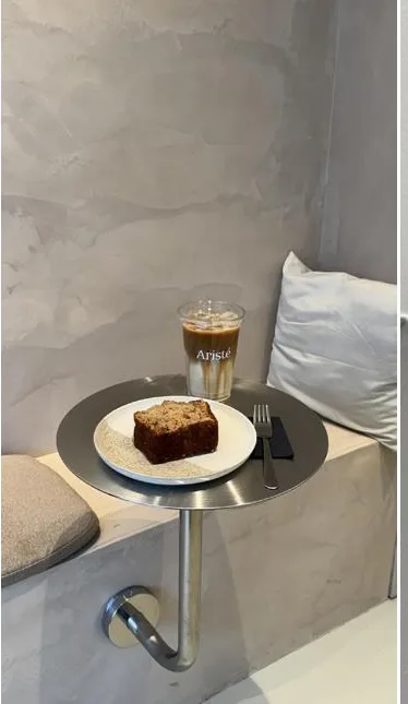 Wandtafel tegen een microcementmuur met een iced latte in een Aristé beker en een plak cake