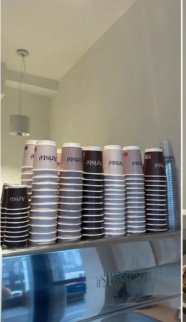 Stapels bruine, roze en crème Aristé bekers boven de espressomachine