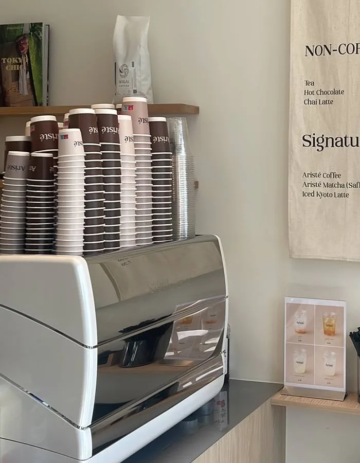 De bar met de espressomachine en stapels bruine en roze Aristé bekers